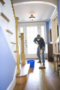 Man mopping wooden floor in bright porch/reception room.